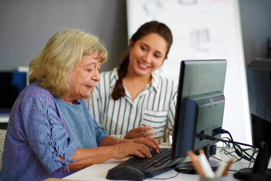 Computer Support Technician Teaching Elderly Woman To Use Her Computer In Her Home